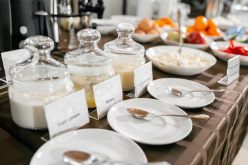 Saucers with spoons in the foreground. Honey, condensed milk, yogurt. Breakfast buffet in hotel.
