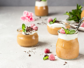 Chocolate mousse with whipped cream, raspberry, mint and pieces of chocolate in portion glasses, light grey background. Happy Valentine’s day.