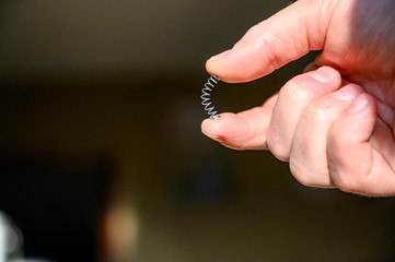 Caucasian hand compressing a metal spring between a thumb and finger