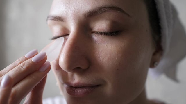 Natural face care with frozen water. The use of ice for the skin against aging and expression wrinkles. Cute Caucasian woman with a towel on her head looks at the camera and moisturizes her skin