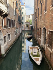 Two old pleasure boats on a leash on the dark dirty water of a narrow canal against the background of dilapidated brick buildings. Sad landscape of the destruction of houses from moisture, flooding .