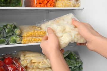 Woman putting plastic bag with cauliflower in refrigerator with frozen vegetables, closeup