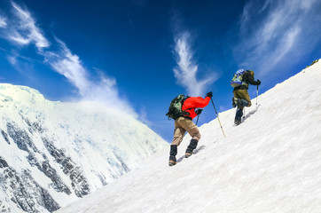 Fototapeta na wymiar Two mountain trekkers on steep snowed hill with dramatic sky background