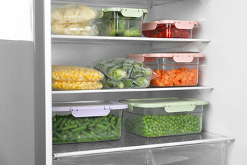 Plastic bags and containers with different frozen vegetables in refrigerator
