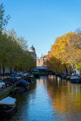 House and boat reflections in the canals of Amsterdam, autumn colors and blue sky