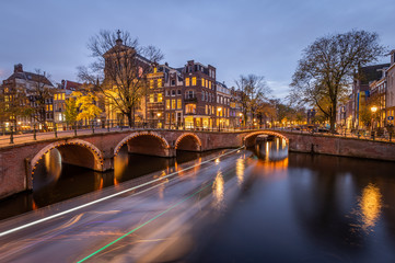 Fototapeta premium Night view of Amterdam cityscape with canal, bridge and medieval houses in the evening twilight illuminated. Amsterdam, Netherlands