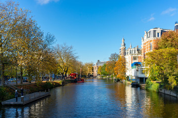 House and boat reflections in the canals of Amsterdam, autumn colors and blue sky