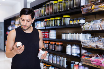 Serious young muscular man  choosing  sport nutrition products in shop