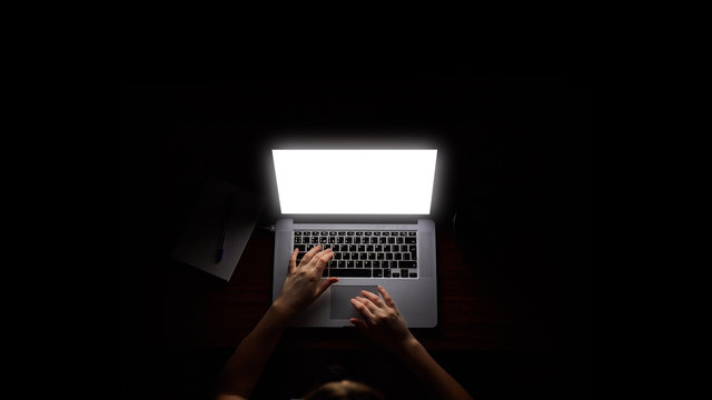 Overhead hacker in the hood working with laptop and mobile phone typing text in dark room