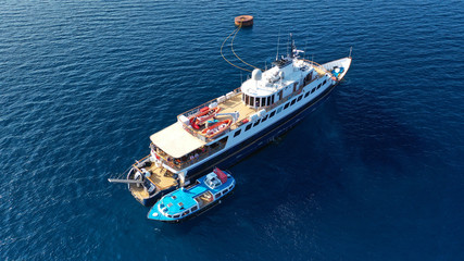 Aerial drone bird's eye top view photo of luxury yacht with wooden deck docked in deep blue waters, Cyclades, Greece
