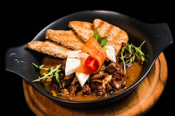 Rustic bowl of cooked beef in sauce, vegetables, decorations and toasted pieces of bread