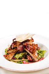 Meal made of green salad,  fresh chicken, crispy bacon nad cheese on top