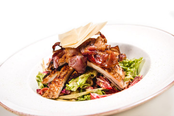 Meal made of green salad,  fresh chicken, crispy bacon nad cheese on top