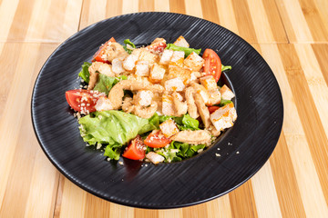 Caesar salad on a black plate, on a wooden background.