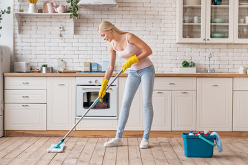 Smiling cleaning service woman with mop cleaning floor in kitchen