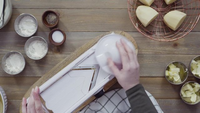 Flat lay. Slicing organic gold potatoes on a V-blade mandoline to prepare scalloped potatoes.