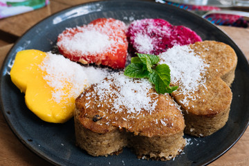 Close up Oatmeal Pancakes and tropical fruits in the form of a heart with mint and honey on wooden table. Valentine's Day. Healthy food concept. Top view.
