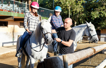 Mature couple with trainer riding horse at farm outdoor