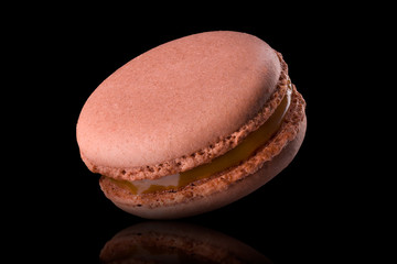 Macro photo of french caramel macaroon with reflection isolated on black