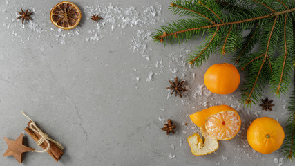 Winter festive composition on a stone grey board with fresh sweet mandarins, one fir branch, anise, cinnamon and artificial snowflakes. With space for text, top view