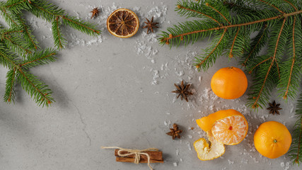 Christmas festive composition on a stone grey board with three fresh mandarins, fir branches, anise, cinnamon and artificial snowflakes. With space for text, top view