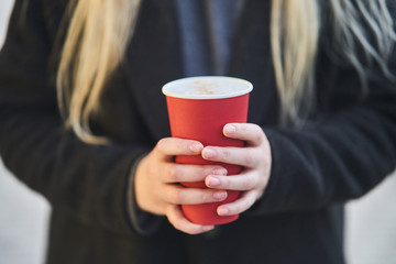 A young girl holds a cup with coffee in her hands. 