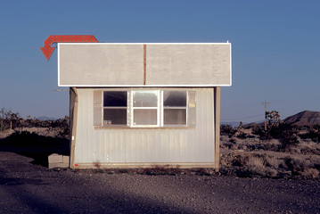 Fototapeta na wymiar Arrow symbol with blank billboard over metallic cottage in desert against sky