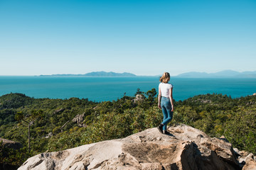 Young stylish independent girl travel the world, sitting on the rock and enjoying the view over the ocean and trees