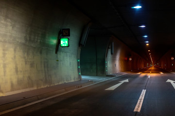 Automobile auto dark car tunnel with white arrows on asphalt showing way direction. Emergency exit sign with many lights. Empty underground vehicle road. Urban abstract city transportation background