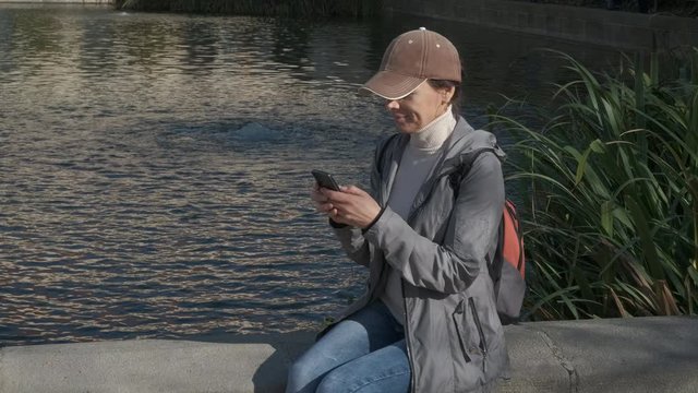 Tourist by a little pond. Girl tourist with a smartphone on the background of a pond in the park.