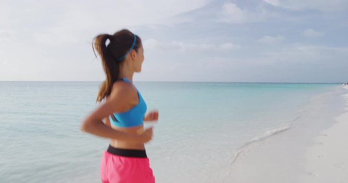 Exercising young woman runner jogging and running on beach happy living healthy aspirational fitness lifestyle. Sporty young Asian Caucasian female in sportswear. REAL TIME STEADICAM RED Camera