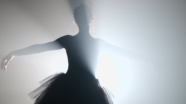 Silhouette of incredible girl dancing ballet in tutu on stage front of spotlight
