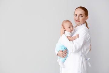 Pediatrician with cute baby on light background