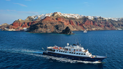 Aerial drone photo of luxury yacht cruising near iconic village of Oia, Santorini island, Cyclades, Greece