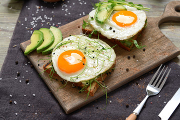 Board with tasty avocado sandwiches with fried egg on table