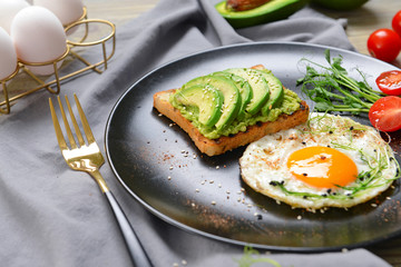 Plate with tasty avocado sandwich and fried egg on table