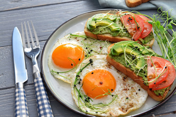 Plate with tasty avocado sandwiches and fried eggs on table