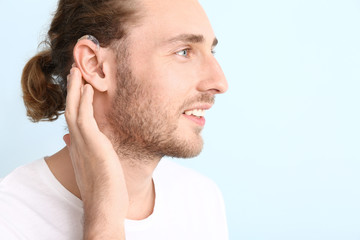 Obraz premium Young man with hearing aid on color background