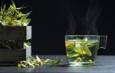 Glass cup of linden tea or blooming tilia with linden blossom on rustic  table. Hot drink winter herbal tea concept, Treatment of cold and flu