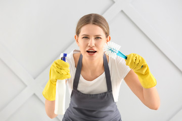 Female janitor with cleaning supplies on grey background