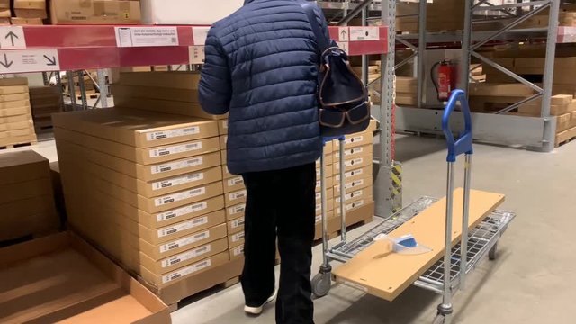 man in a jacket carries a large shopping trolley in a self-service furniture store, a shopping concept