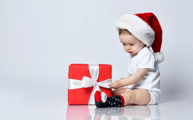 Infant baby boy toddler sitting in christmas cap and xmas present gift box playing white t-shirt 