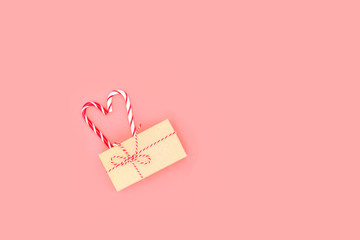 Gift box on pink background. Two lollipops are connected in the heart. Candy heart.Christmas striped candy canes.Top view