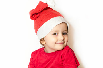 Portrait little happy girl in festive clothes, santa claus hat in white. Cute child in Christmas clothes is waiting for the holiday. beautiful baby in red dress is smiling and looking at the camera.