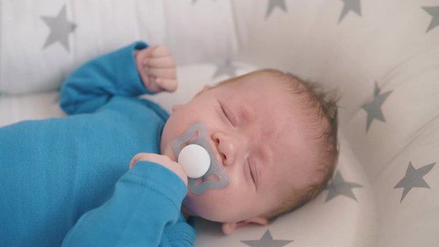 cute little baby with hypertonicity problem cries sucking dummy while sleeping in cocoon decorated with stars close view
