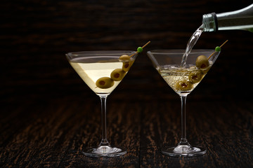 Pouring martini from the bottle into the glass against  wooden background.