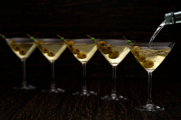 Pouring martini from the bottle into the glass against wooden background.