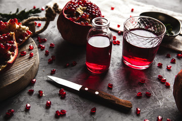 Red pomegranate juice in a glass, ripe and cut pomegranate and a sprig of mint on a gray concrete background. Vitamin, antioxidant and health food concept. Flat lay.Top view.