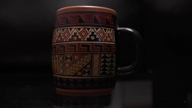 Cup with Inca drawings with dark background and glass table