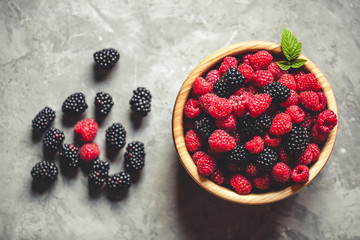 raspberries and blackberries in wood bowl on gray table, vintage